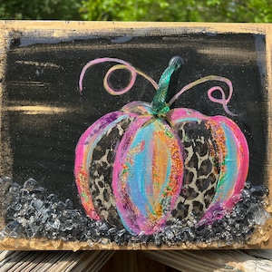 May include: A colorful, glittery pumpkin with a leopard print design on a black background. The pumpkin is painted in shades of pink, blue, and green, and has a glittery finish. The background is black with a gold border. The pumpkin is surrounded by clear glass beads.
