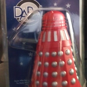 May include: A red and silver Doctor Who Dalek figure from the popular British science fiction television series. The figure is packaged in a clear plastic blister pack with a blue and white background featuring the Doctor Who logo and the words "Another Famous Doctor Who Figure from" and "D.A.R.L.E.K."