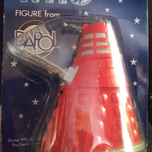 May include: A red and silver Doctor Who Dalek figure from Palitoy. The figure is packaged in a blue and silver blister pack with stars and the text "Another Famous Doctor Who Figure from Palitoy".