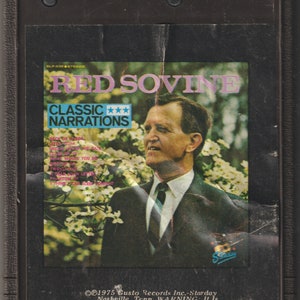 May include: A vintage cassette tape featuring a photo of Red Sovine, a country music singer, with the text "Red Sovine Classic Narrations" and a list of song titles. The cassette tape is black with a silver label.