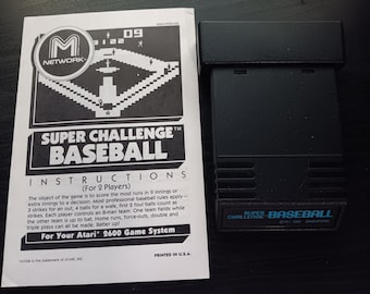 May include: A black Atari 2600 game cartridge with a blue label that reads "Super Challenge Baseball" and "C MI 1982 SINGAPORE". The cartridge is next to a black and white instruction manual with the title "Super Challenge Baseball" and instructions for the game.