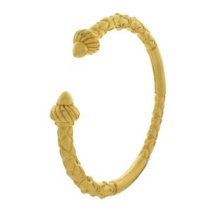 May include: A gold-colored cuff bracelet with intricate detailing. The open-ended design features decorative finials and textured patterns along the band. The bracelet's design includes floral and geometric elements.