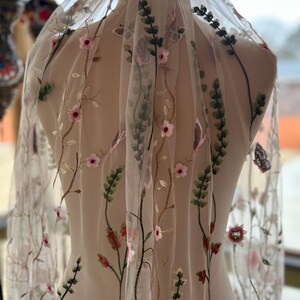 May include: White tulle fabric with embroidered floral designs in shades of pink, green, and brown. The flowers are delicate and intricate, and the fabric is sheer and lightweight.