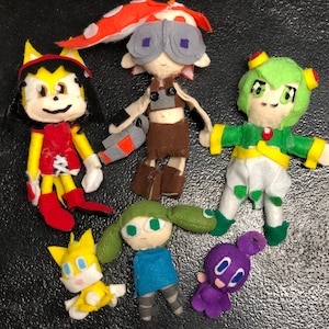 Puede incluir: Una colección de peluches, incluyendo un erizo amarillo y rojo, un personaje verde y amarillo con una flor en la cabeza, un personaje morado con una flor en la cabeza, un personaje azul con una flor en la cabeza y un personaje amarillo y naranja con una flor en la cabeza.