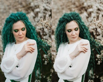 May include: A person with vibrant teal hair and matching eye makeup, wearing a white dress with a green and white accent. The person is set against a backdrop of white blossoms, creating a soft, natural aesthetic.