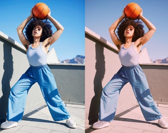 May include: A person in a light blue vest top and wide-leg blue trousers holds an orange basketball overhead. The person is standing outside on a sunny day, with a clear blue sky in the background. White trainers complete the outfit.