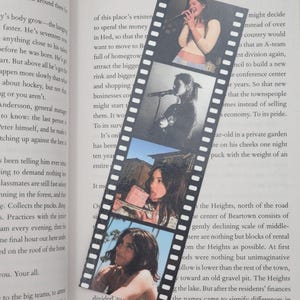 May include: A bookmark featuring a film strip design with four black and white images of a woman. The images show the woman singing into a microphone and posing. The bookmark is placed on top of an open book.