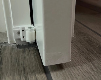 May include: Close-up of a white door and frame with a white hinge and a white cylindrical door stop. The door and frame are set against a wood-look floor.