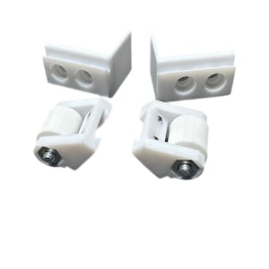 May include: Four white plastic parts for a sliding door system. Two of the parts are L-shaped brackets with two holes each. The other two parts are rollers with a metal axle.