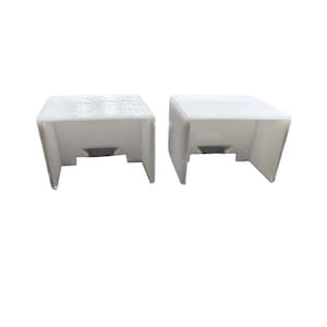 May include: Two white plastic rectangular blocks with a small opening in the center of each block.