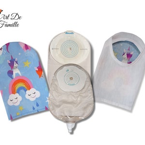 Peut inclure: Un ensemble de trois fournitures d'ostomie, comprenant une poche transparente avec un drain, une plaque adhésive blanche et une housse en tissu bleu avec un arc-en-ciel et une licorne. La housse en tissu porte le texte "Art De Famille".