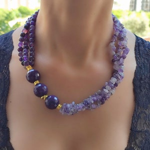 May include: A multi-strand necklace made of amethyst beads in various sizes and shapes. The necklace features a graduated design with larger, round beads at the front and smaller, irregular beads at the back. The beads are a deep purple colour and are accented with gold-toned spacers.