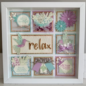 May include: A white frame with a collage of paper crafts inside. The collage features hummingbirds, flowers, and inspirational quotes like "Hello beautiful", "Relax", "You are beyond incredible", and "The good things in life are better with you".