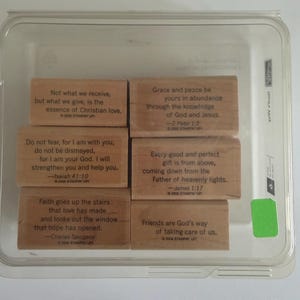 May include: A set of six rectangular wooden rubber stamps housed in a clear plastic container. Each stamp features a different inspirational quote and citation, including verses from the Bible and a quote by Charles Spurgeon, all dated 2006.