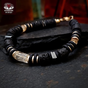May include: Black lava rock bracelet with gold-colored accents and clear, rectangular crystal beads. The bracelet features silver-colored metal bars and the text "HANDMADE IN ITALY" with a heart logo.