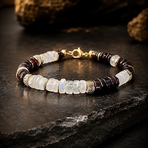 Könnte beinhalten: Ein Perlenarmband mit abwechselnden Segmenten aus durchscheinenden weißen Mondstein-Scheiben und dunkel rotbraunen Granat-Scheiben. Das Armband ist mit kleinen goldfarbenen Metall-Abstandshaltern und einem goldfarbenen Karabinerverschluss versehen.