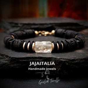 May include: Black lava rock bead bracelet with gold-tone accents and a clear, rectangular gemstone. The bracelet is handmade and features the text "JAJAITALIA Handmade Jewels" and the signature "Giulia Torelli".