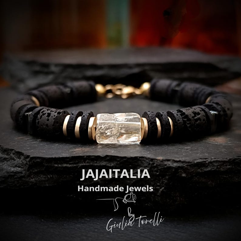 May include: Black lava rock bead bracelet with gold-tone accents and a clear, rectangular gemstone. The bracelet is handmade and features the text "JAJAITALIA Handmade Jewels" and the signature "Giulia Torelli".