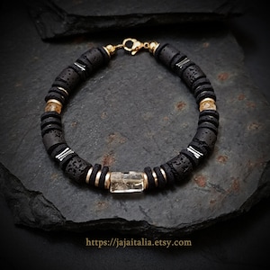 May include: A black beaded bracelet with gold accents and a rectangular, clear stone centerpiece. The bracelet features dark gray, circular beads, gold-colored spacers, and a gold clasp. The Etsy shop URL is visible at the bottom.