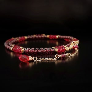 Può includere: Una delicata collana a catena dorata con un ciondolo di pietra rossa. La collana è realizzata con piccole perle rosse e dorate.