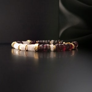 Può includere: Un braccialetto fatto di perline bianche e rosso scuro con accenti dorati.