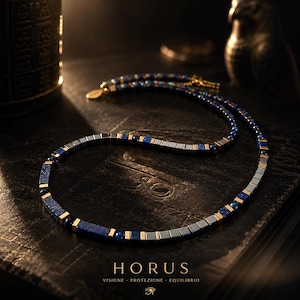 Può includere: Una collana con perline alternate in lapislazzuli blu scuro, perline quadrate grigio metallizzato e piccoli distanziatori dorati. Il gioiello è appoggiato su una superficie scura con il testo HORUS, VISIONE, PROTEZIONE, EQUILIBRIO stampato sotto.