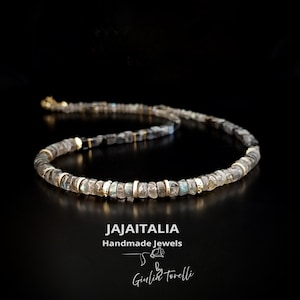 K&ouml;nnte beinhalten: Halskette mit kleinen, unregelm&auml;&szlig;ig geformten, grauen und klaren Perlen, die mit goldfarbenen Abstandshaltern versehen sind. Der Hintergrund ist schwarz. Der Text "JAJAITALIA Handmade Jewels" und die Signatur "Giulia Torelli" sind sichtbar.