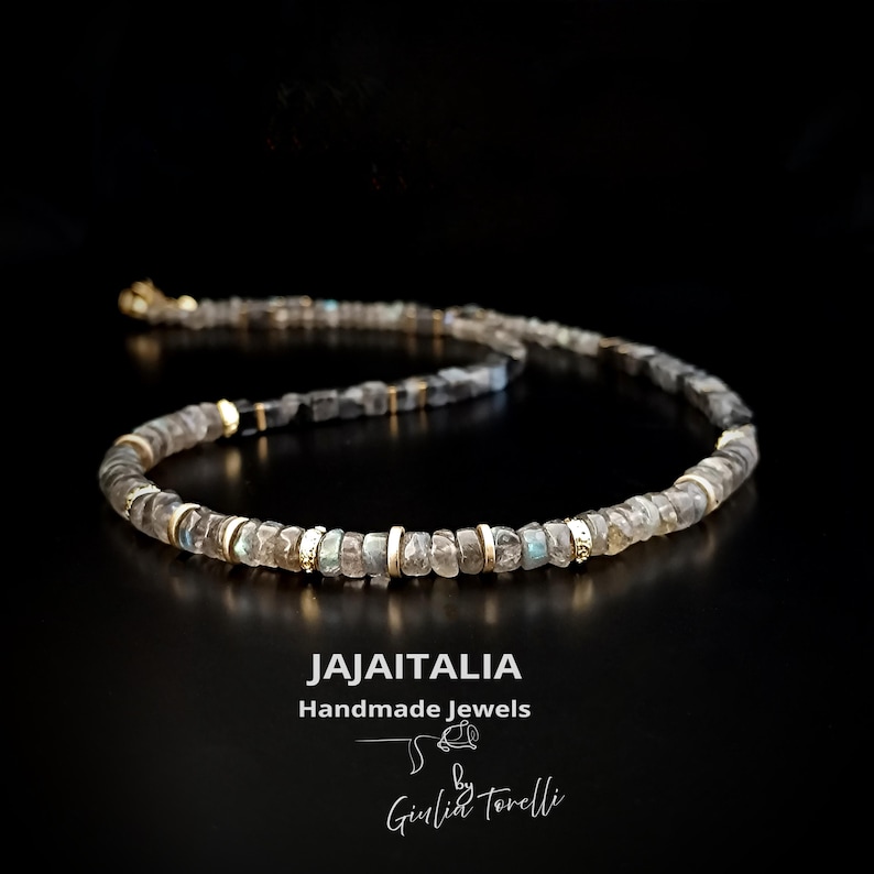 K&ouml;nnte beinhalten: Halskette mit kleinen, unregelm&auml;&szlig;ig geformten, grauen und klaren Perlen, die mit goldfarbenen Abstandshaltern versehen sind. Der Hintergrund ist schwarz. Der Text "JAJAITALIA Handmade Jewels" und die Signatur "Giulia Torelli" sind sichtbar.