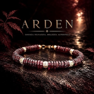 May include: A bracelet featuring dark red, disc-shaped beads interspersed with four ornate gold-toned metal spacers. The piece includes a gold-toned lobster claw clasp. The text ARDEN and ESSENZA SELVAGGIA, BELLEZZA AUTENTICA is visible above.