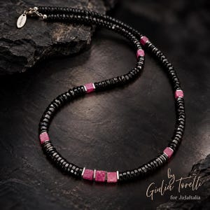 May include: A beaded necklace featuring small, faceted black circular beads interspersed with square-shaped pink stones and silver-toned metal spacers. The necklace includes a silver-toned metal clasp with a small tag labeled Giulia Torelli.