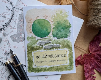 May include: Watercolor greeting card featuring a green hobbit door with the words "no admittance except on party business." The card is surrounded by greenery and stone steps. A map and fountain pen are also visible.