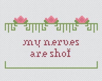 May include: Cross-stitch artwork in a wooden frame. The design features pink flowers above the text "my nerves are shot" in a red-brown color. Green decorative elements and a green line complete the design.