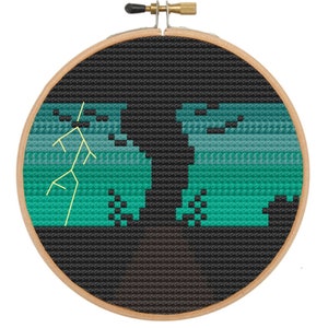 Può includere: Un ricamo a punto croce nero e verde con il disegno di un albero con un fulmine in un telaio da ricamo in legno.