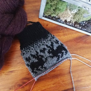 May include: A close-up of a black and grey knitted sock with a geometric pattern. The sock is being worked on with red and white yarn.