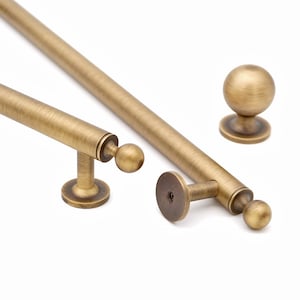 May include: A set of antique brass cabinet hardware, featuring two bar pulls, two knob pulls, and a round knob. The hardware has a vintage aesthetic with a warm, aged finish. The pulls have a cylindrical design with ball-shaped ends.