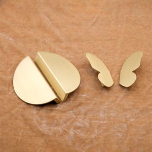 May include: Three gold-toned metal cabinet pulls. Two are half-circle shapes that fit together. The third is a butterfly shape.