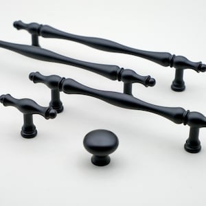 Op de afbeelding: Een set van vijf zwarte kastknoppen en -grepen. De set bevat drie verschillende stijlen grepen en één knop. De grepen zijn allemaal van metaal en hebben een matzwarte afwerking.
