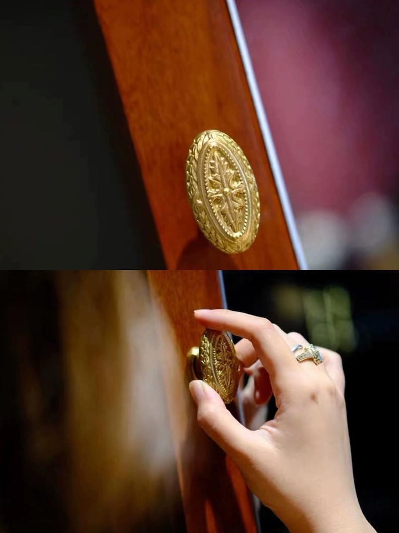 K&ouml;nnte beinhalten: Ein ovaler T&uuml;rknauf in Goldton mit aufwendigen floralen Mustern. Der Knauf ist an einer Holzt&uuml;r befestigt.