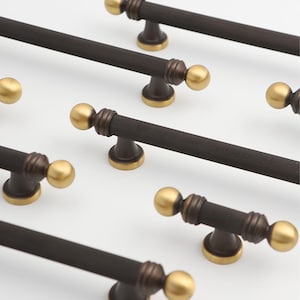 May include: A set of six cabinet pulls with a textured black finish and gold accents. The pulls have a round knob on each end.