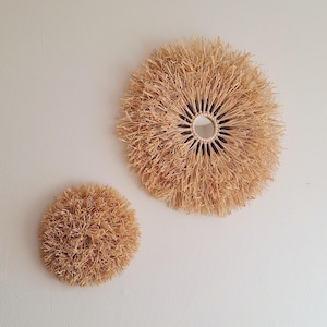Peut inclure: Deux décorations murales circulaires en paille de couleur naturelle. L'une est grande avec une ouverture centrale, l'autre est plus petite. Elles sont fixées sur un mur blanc, ajoutant une touche rustique.