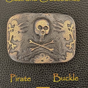 May include: A bronze-colored pirate buckle with a skull and crossbones design. The buckle is embossed with floral details and the words "Pirate Buckle".