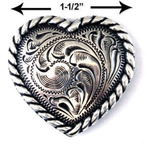 May include: Silver heart-shaped belt buckle with a rope-like border and an intricate engraved design. The buckle measures 1-1/2 inches in diameter.