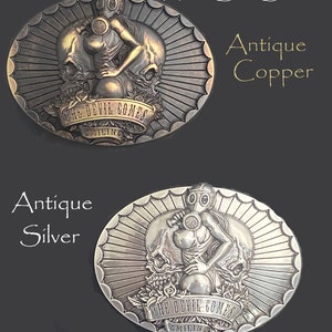 May include: Antique oval belt buckle with a 3D design. The buckle features a woman in a gas mask standing between two skulls. The buckle is available in copper and silver finishes. The text "The Devil Comes Smiling" is engraved on the buckle.