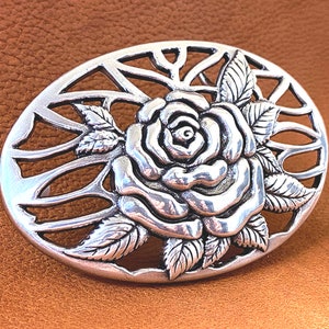May include: Silver-toned belt buckle with a detailed rose design and a cut-out background.