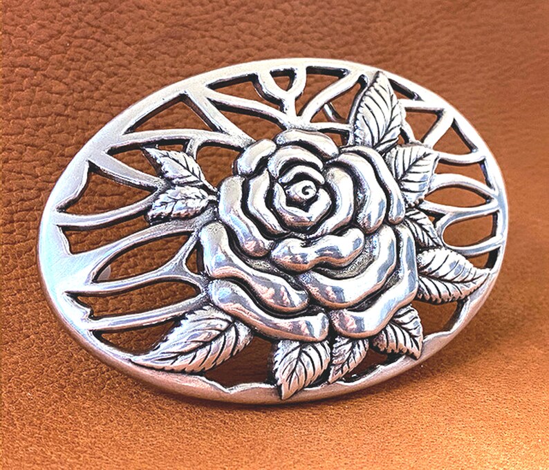 May include: Silver-toned belt buckle with a detailed rose design and a cut-out background.