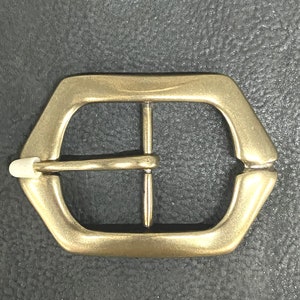 May include: A gold-toned metal belt buckle with a hexagonal shape and a smooth, polished finish.