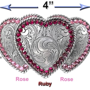 May include: Silver-toned heart-shaped belt buckle with intricate floral engraving and a ruby-colored center heart. The buckle is 4 inches wide and 2-3/8 inches tall, with rose-colored accents. A decorative accessory.
