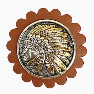 May include: A round, brown leather patch with a scalloped edge, featuring a silver and gold-toned metal emblem. The emblem depicts a Native American chief in profile, wearing a feathered headdress. The design is detailed and ornate.