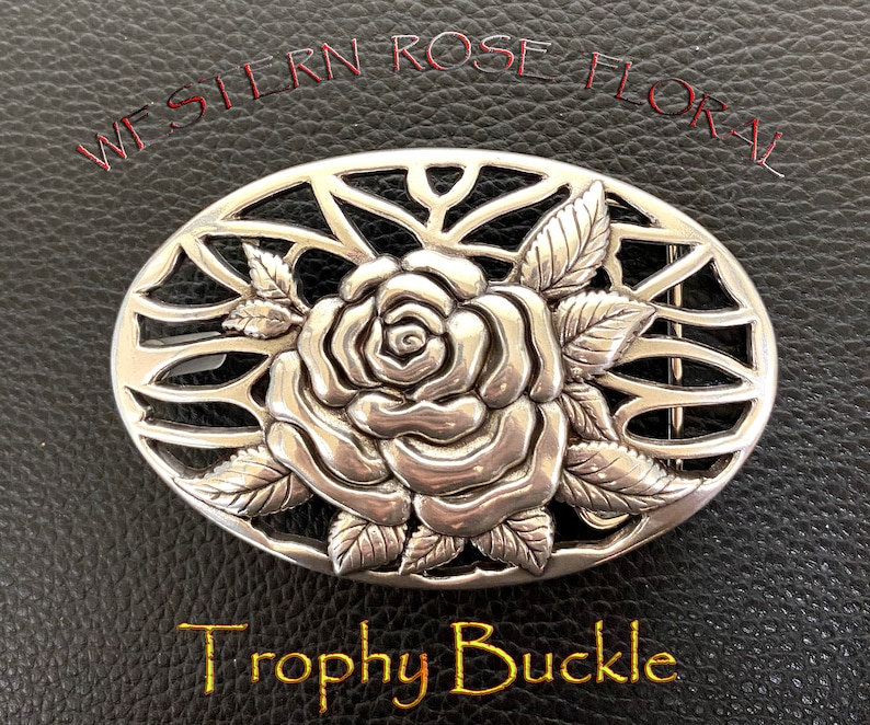 May include: Silver belt buckle with a detailed rose design and a filigree background. The buckle is oval shaped and says "Western Rose Floral Trophy Buckle".