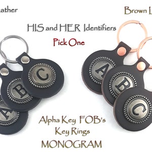 May include: Three leather keychains with metal key rings. Each keychain has a round leather tag with a silver metal circle featuring a letter, A, B, or C. The text "HIS and HER Identifiers" and "Pick One" is above the keychains. The text "Alpha Key FOB's Key Rings MONOGRAM" is below the keychains.
